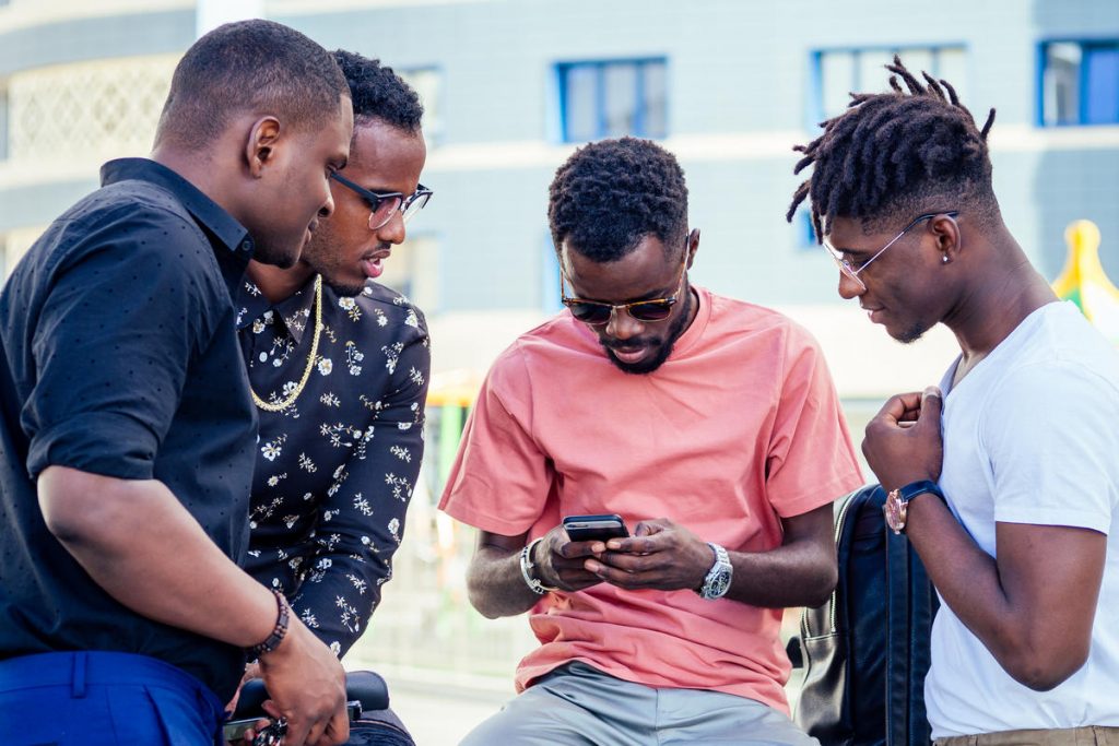 a group of four fashionable cool African American guys students communicating on the street looking at smartphone video games